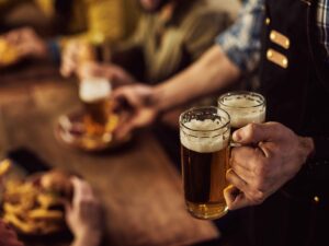 Garçom segurando duas canecas de cerveja artesanal em bar com clientes desfocados ao fundo