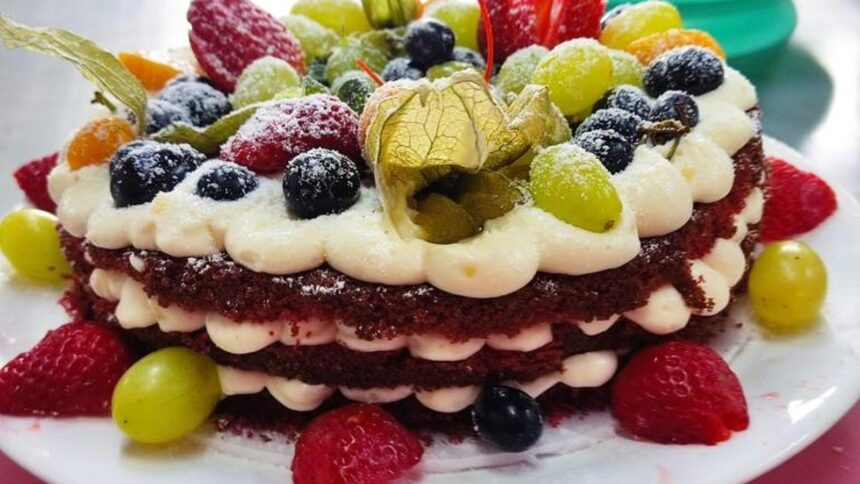 Bolo de camadas com massa escura e creme branco, decorado com frutas frescas e açúcar de confeiteiro