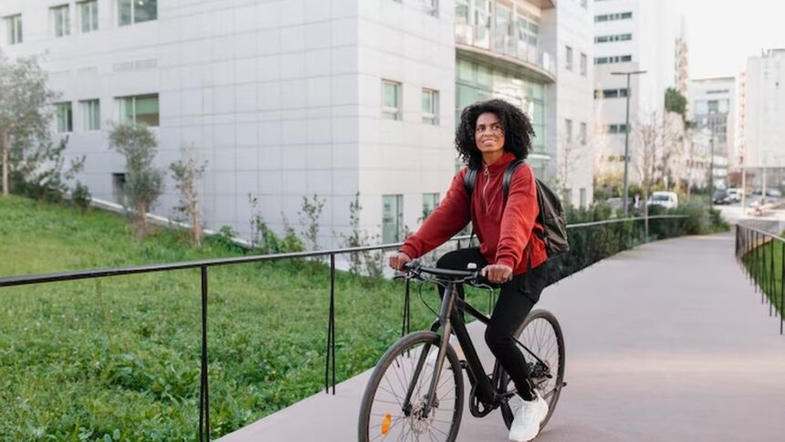Mulher jovem com mochila e casaco vermelho pedala bicicleta preta em caminho urbano