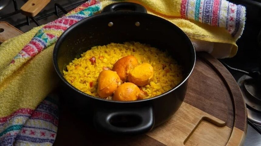 Panela com arroz amarelo e quatro pequis inteiros, sobre tábua de madeira