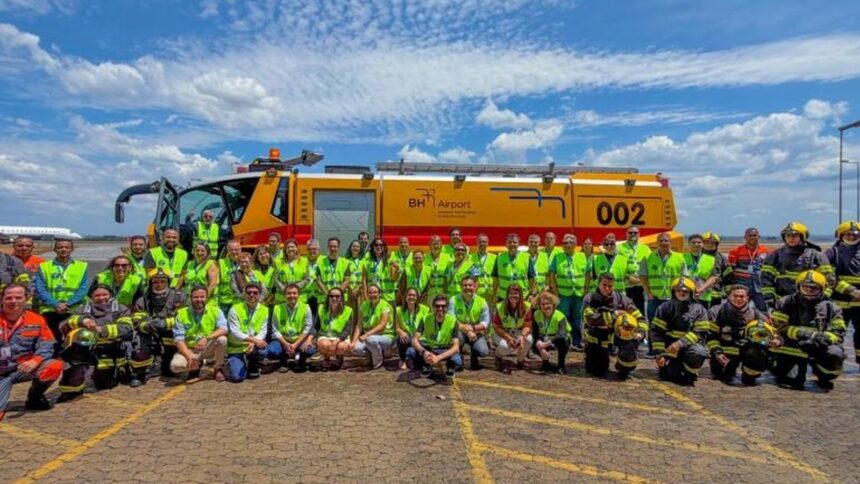 Grupo de pessoas, algumas de coletes e bombeiros, posam em frente a caminhão BH Airport