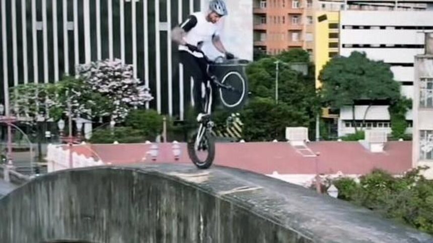 Ciclista em capacete se equilibra em bicicleta trial na borda de viaduto urbano