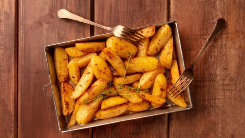 Batatas assadas temperadas em assadeira de metal sobre mesa de madeira com dois garfos