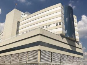 Edifício hospitalar moderno, fachada clara, vidro curvo e céu azul com nuvens brancas