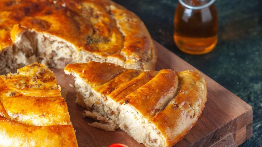 Torta de carne moída assada, cortada em fatias, sobre uma tábua de madeira escura