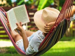Pessoa de chapéu de palha e roupa branca lendo livro em rede colorida ao ar livre