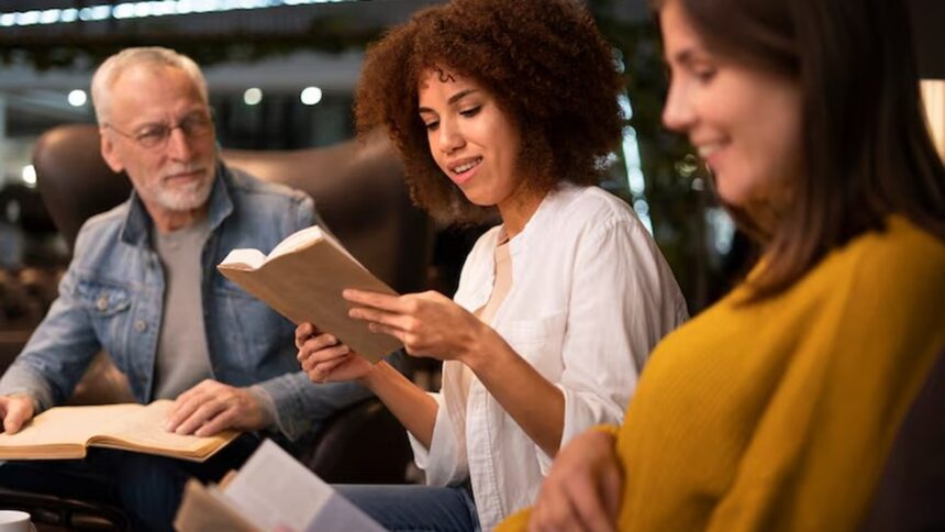 Homem idoso de óculos e duas mulheres jovens leem livros em ambiente interno