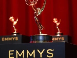 Três troféus dourados do Emmy em pedestais pretos com EMMYS, sobre um fundo vermelho