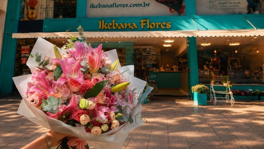 Mão segura grande buquê de lírios rosa em frente à fachada da floricultura Ikebana Flores