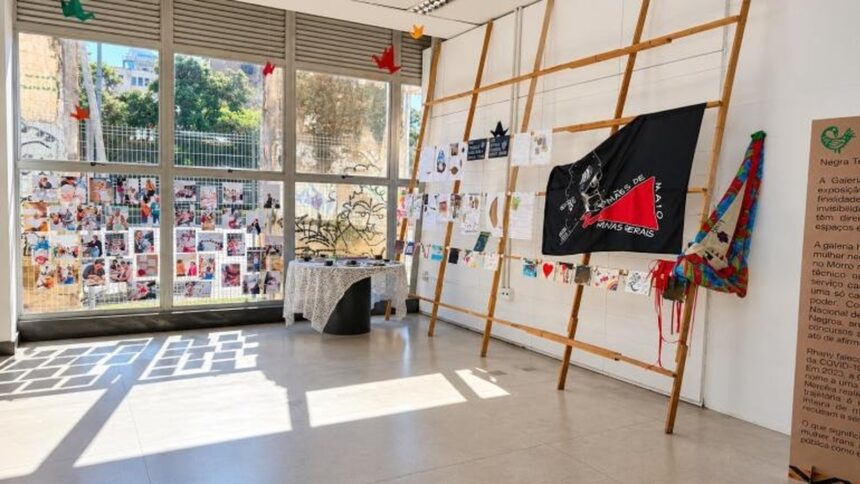 Exposição Mães de Maio em galeria: janelas com fotos, mesa e bandeira preta