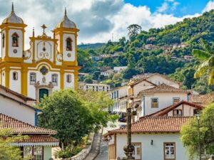Vista panorâmica de Ouro Preto com igreja barroca amarela e branca, casarões coloniais e morros verdes