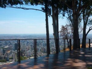Deck de madeira, guarda-corpo, árvores altas e vista da cidade de Belo Horizonte.