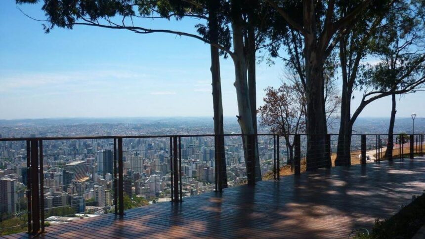 Deck de madeira, guarda-corpo, árvores altas e vista da cidade de Belo Horizonte.