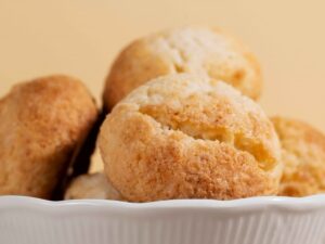 Vários pães de queijo redondos e dourados em uma tigela branca sobre fundo claro