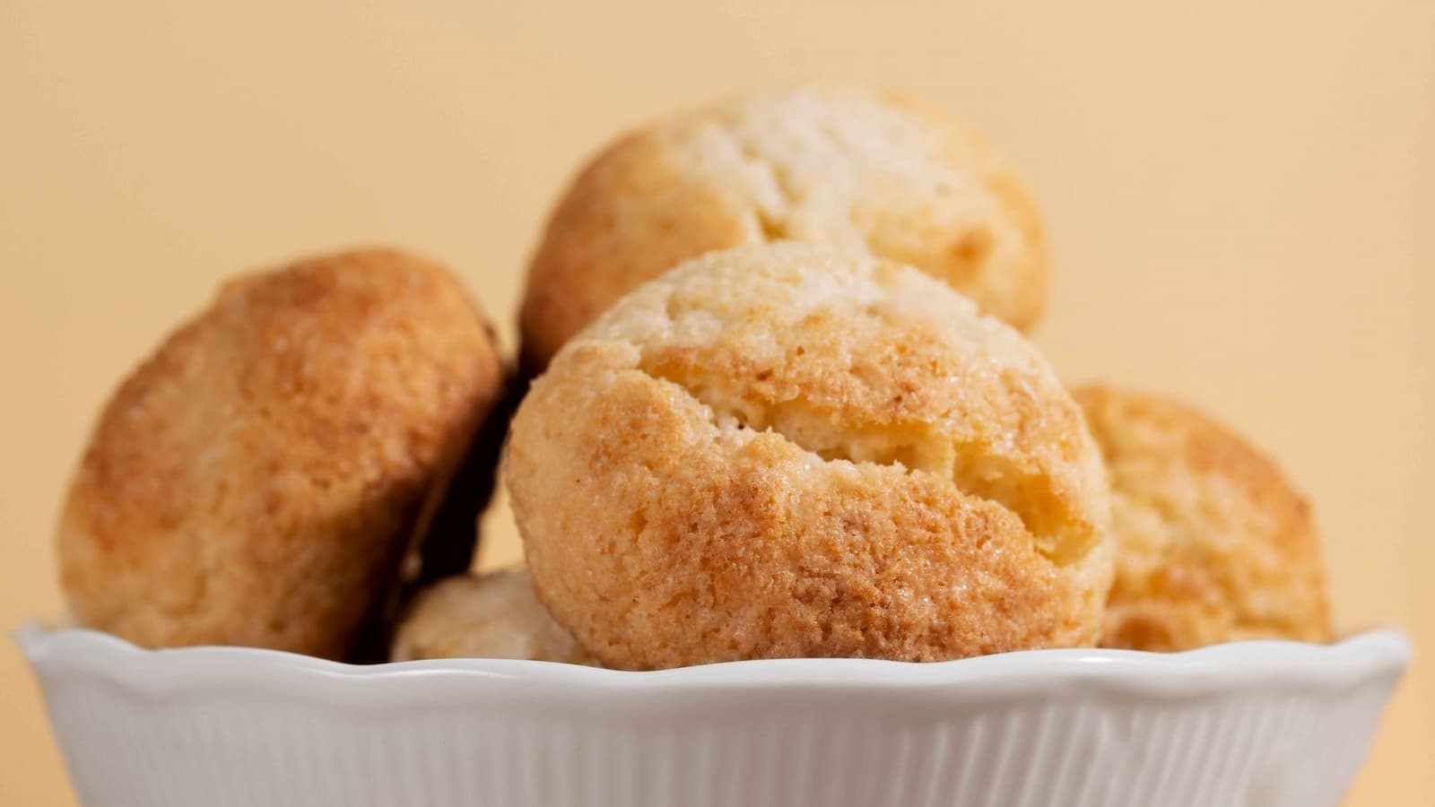 Vários pães de queijo redondos e dourados em uma tigela branca sobre fundo claro