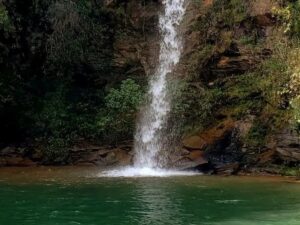 Cachoeira em rocha com vegetação verde abundante, desaguando em poço de água esverdeada