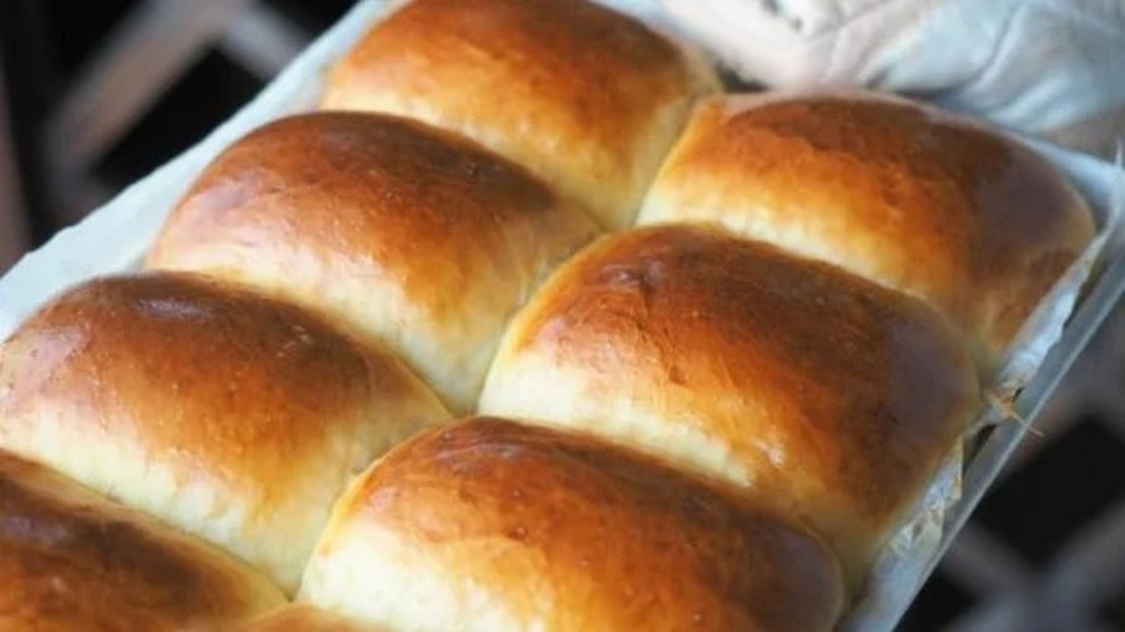 Pães dourados assados, arranjados em fileiras, dentro de uma assadeira retangular forrada