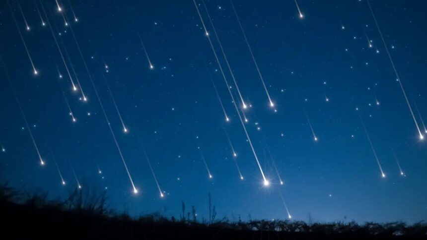 Céu noturno azul-escuro com múltiplas trilhas luminosas de meteoros caindo sobre uma paisagem escura.