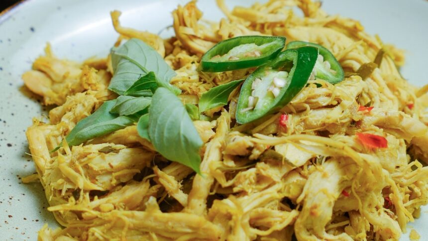 Frango desfiado amarelado em prato claro, com folhas verdes e rodelas de pimenta verde