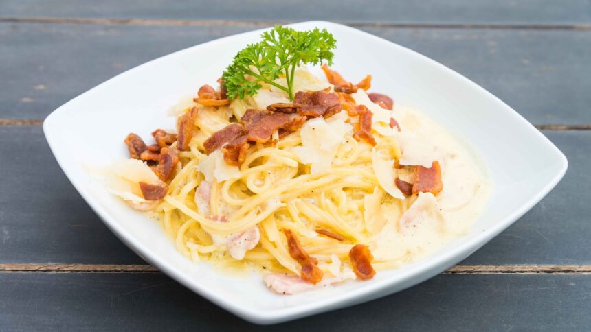 Prato de espaguete carbonara com bacon, queijo e salsa fresca em mesa de madeira escura