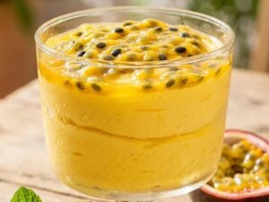 Copo de mousse de maracujá cremoso com polpa e sementes frescas; um maracujá cortado