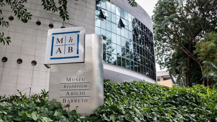 Placa do Museu Histórico Abílio Barreto e prédio com fachada de vidro, cercado por plantas
