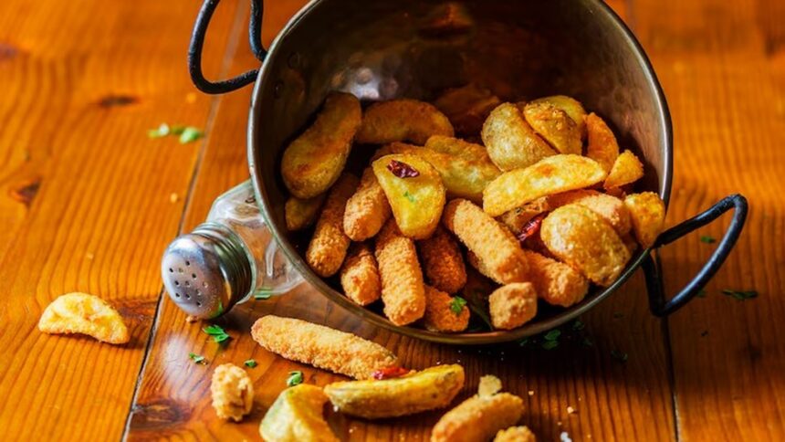 Frituras variadas, incluindo batatas e empanados, derramadas de tigela metálica em mesa de madeira