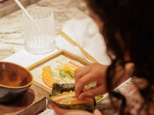 Mãos infantis montam temaki com nori, salmão e pepino em uma oficina de culinária