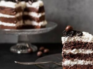 Fatia de bolo de chocolate com camadas de creme branco, decorada com bola de chocolate, bolo desfocado ao fundo