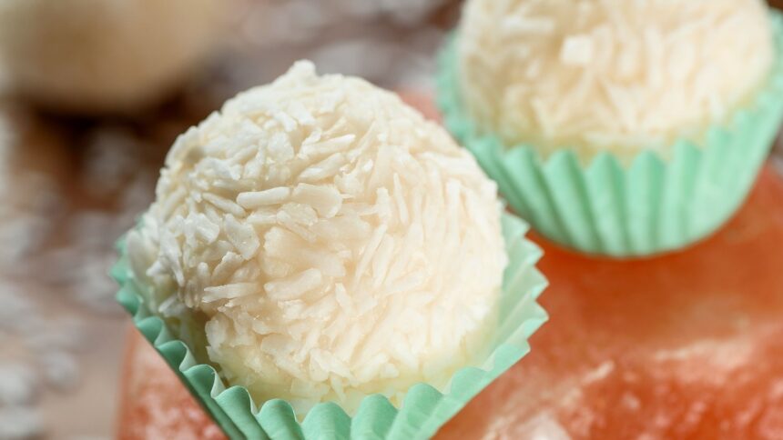 Duas trufas de coco brancas em forminhas verdes claras, uma em foco nítido