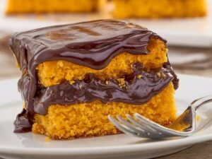 Fatia de bolo de cenoura com cobertura de chocolate em prato branco e garfo
