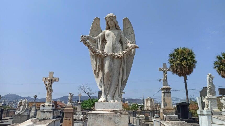Estátua de anjo em mármore branco com asas e guirlanda em cemitério sob céu azul