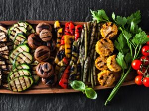 Tábua de madeira com vegetais grelhados: berinjela, abobrinha, cogumelos, pimentões, aspargos, milho, tomate e salsinha