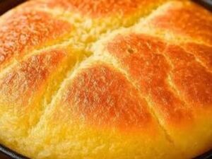 Pão redondo dourado-alaranjado em uma frigideira preta com textura rústica na superfície