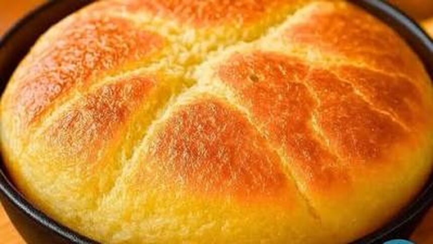 Pão redondo dourado-alaranjado em uma frigideira preta com textura rústica na superfície