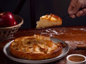Mão serve fatia de bolo de maçã e canela com maçãs e especiarias na mesa