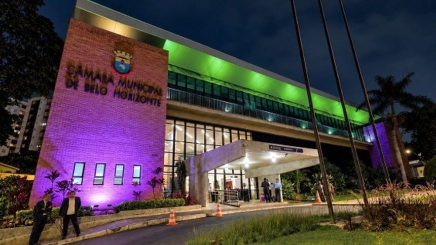 Fachada da Câmara Municipal de Belo Horizonte iluminada em roxo e verde à noite.