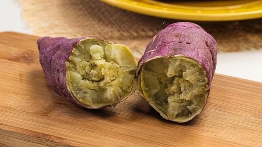 Duas metades de batata-doce roxa cozida e macia sobre tábua de madeira clara