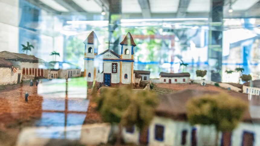 Maquete de um povoado colonial com igreja central de duas torres, casas e figuras em miniatura