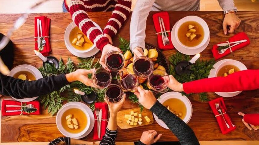 Pessoas em uma mesa de madeira brindando com vinho tinto em confraternização festiva