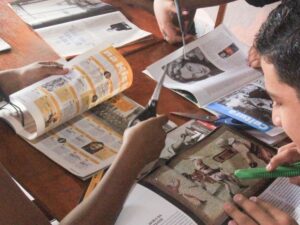 Mãos recortam revistas e jornais com tesouras e estilete em uma mesa de madeira