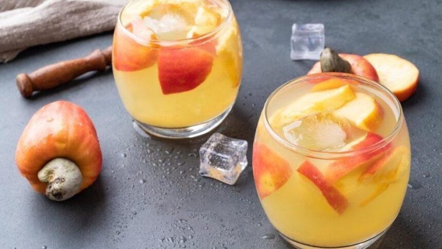 Dois copos de drink de caju com gelo, fatias, caju fresco e pilão