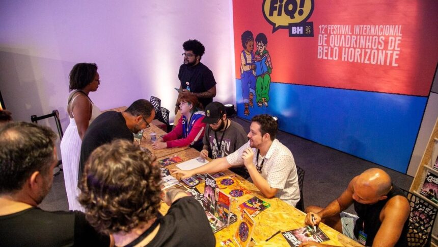 Autores autografam quadrinhos para fãs em mesa durante o Festival FIQ BH, com banner ao fundo