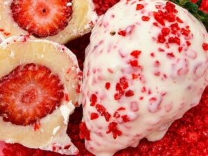 Morango coberto com chocolate branco e granulado vermelho, ao lado de morangos recheados cortados