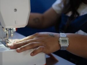 Close-up de mão com relógio digital costurando tecido em máquina de costura branca