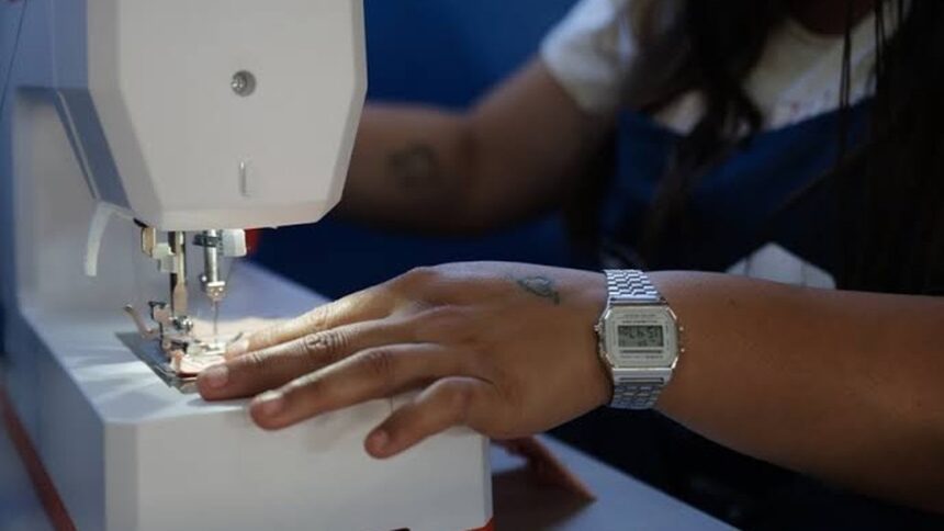 Close-up de mão com relógio digital costurando tecido em máquina de costura branca