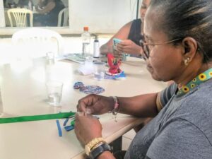 Mulher de óculos, sentada à mesa, fazendo artesanato com pedaços de tecido colorido