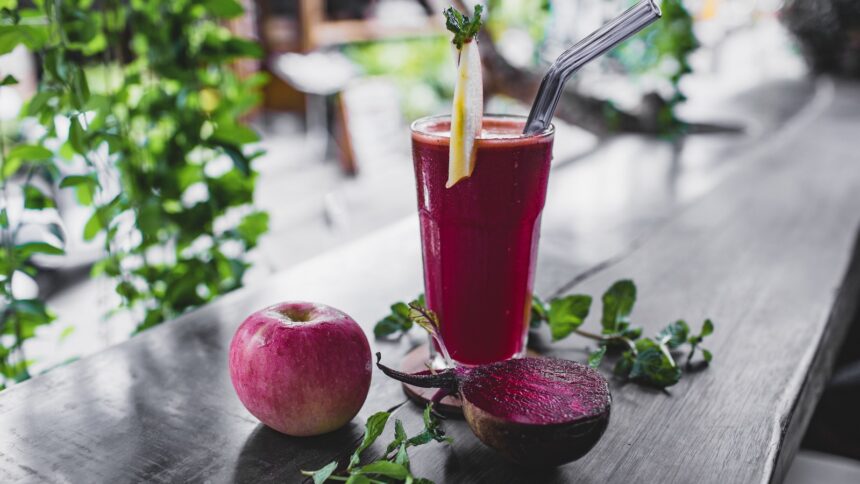 Copo de suco vermelho com palha de metal, maçã, beterraba cortada e hortelã na mesa de madeira