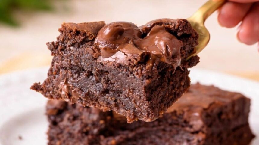 Um pedaço de brownie de chocolate úmido com calda sendo levantado por uma colher dourada