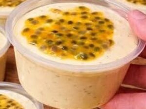 Mão segura pote transparente de mousse de maracujá com sementes e polpa